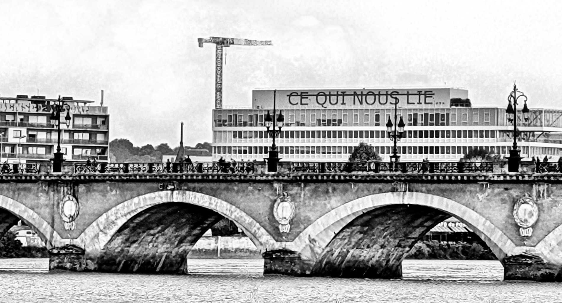 Image of a bridge with 'Ce qui nous lie' appearing on a building in the background