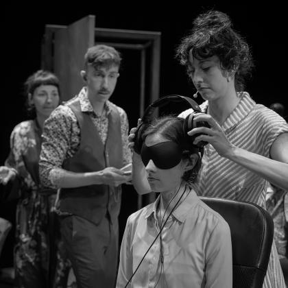 Une femme met des écouteurs à une autre femme qui porte un bandeau sur les yeux. Deux personnes, à leur droite, les regardent.
